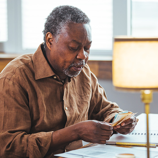 Sad senior African American man sitting at table with laptop, feeling pressure because of payment problem, feeling anxious over money. Senior man calculating his disability pension