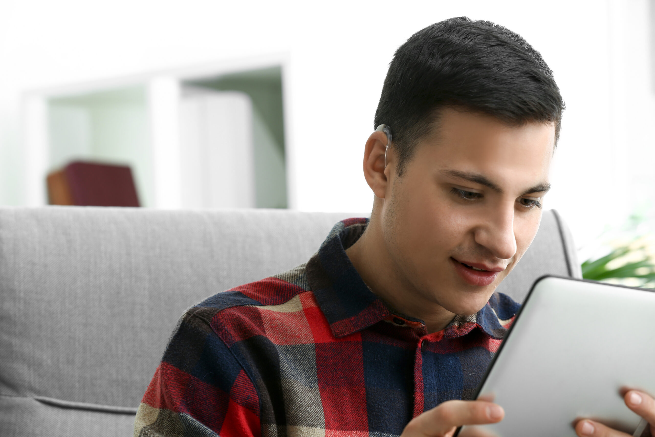 Young,Man,With,Hearing,Aid,Using,Tablet,Computer,At,Home