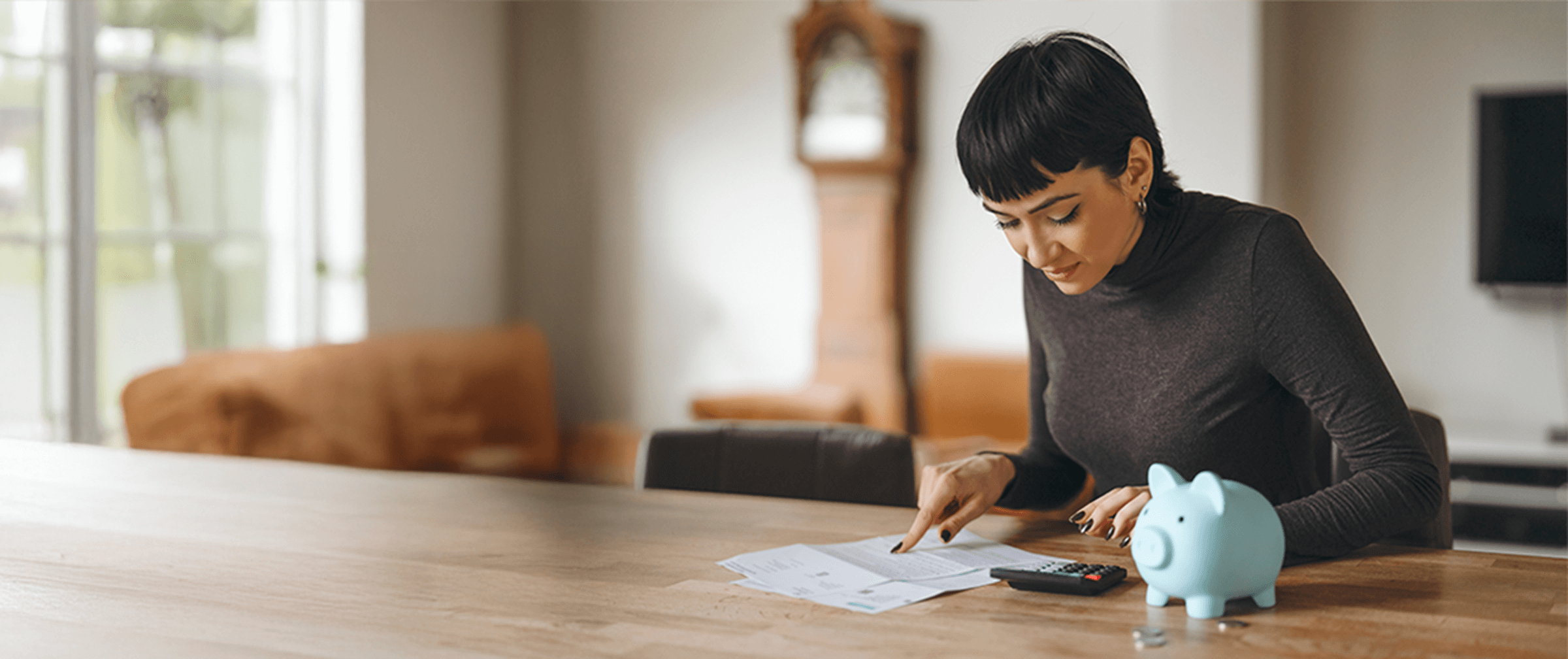 Person sitting at a wooden table reviewing finances with a calculator and a piggy bank