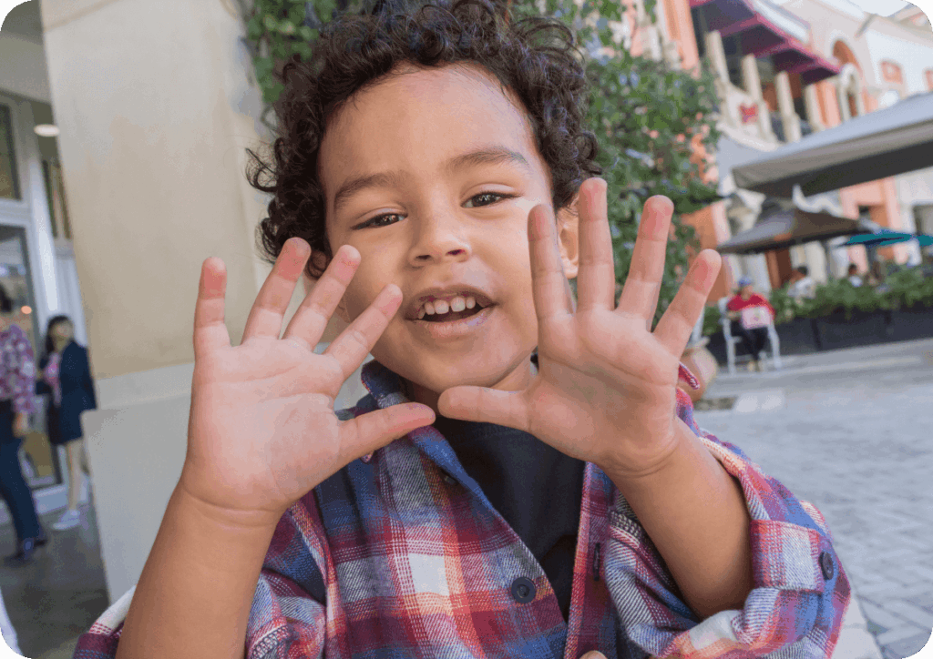 Child outdoors, holding up both hands showing the number 10.