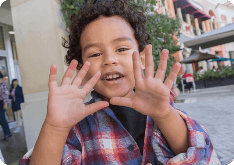 Child outdoors, holding up both hands showing the number 10.
