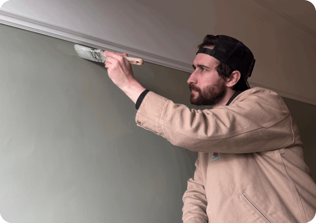 Dan Barker painting a wall, wearing a beige jacket and a backwards cap