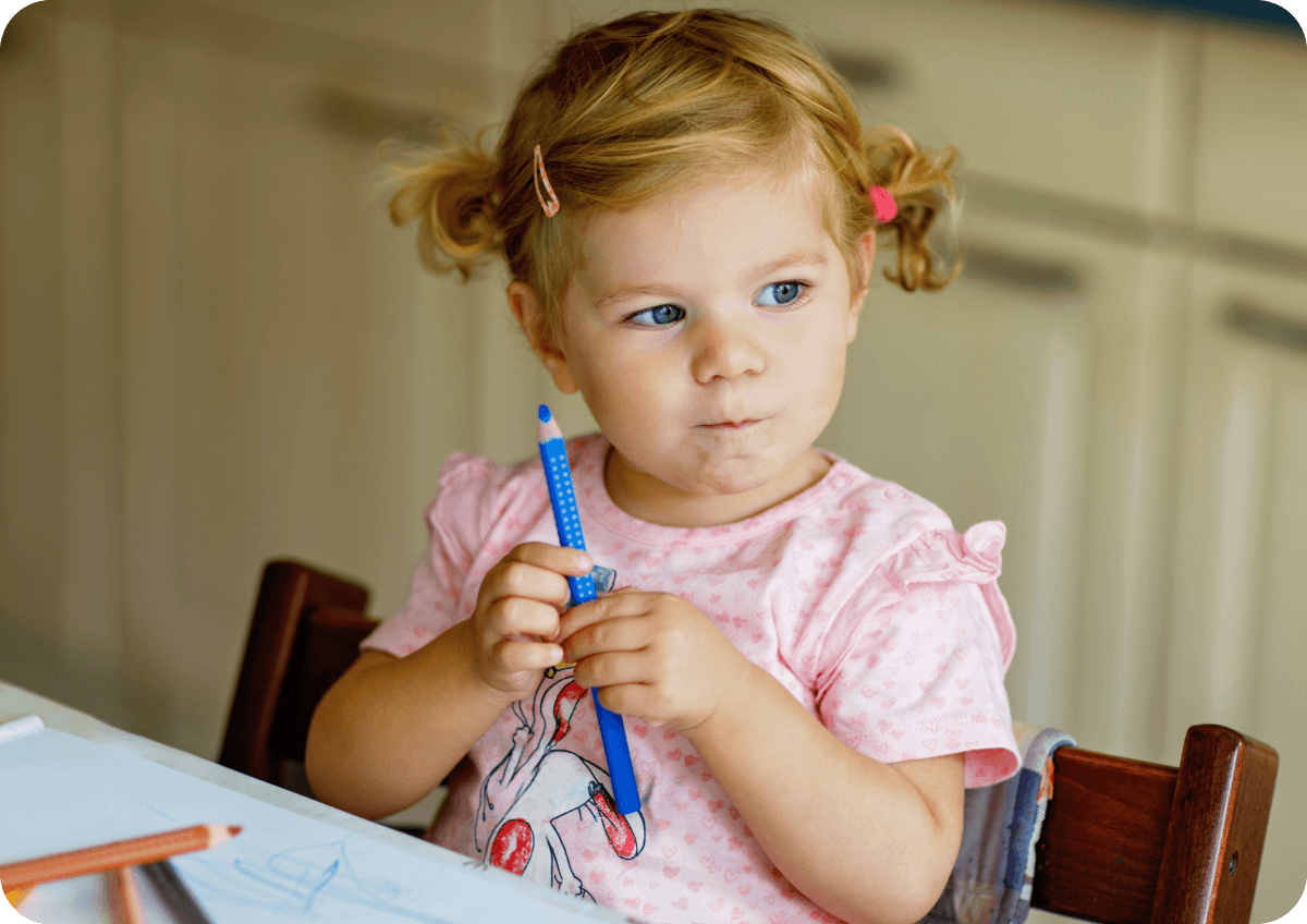 Young child sitting at a table thinking and holding pencil.