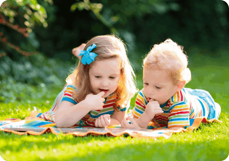 Two children lying on a blanket in the garden, wearing matching striped shirts.