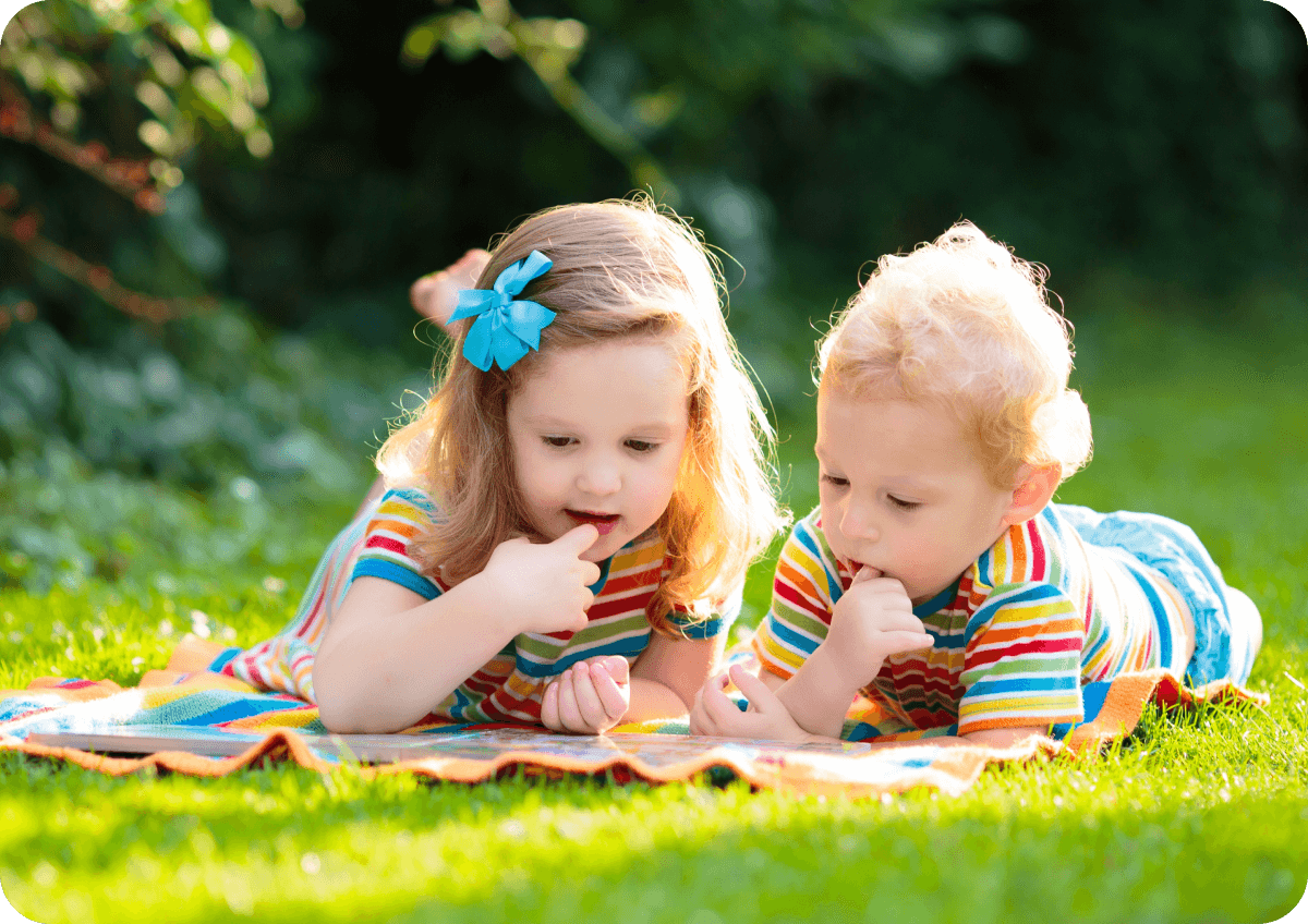 Two children lying on a blanket in the garden, wearing matching striped shirts.