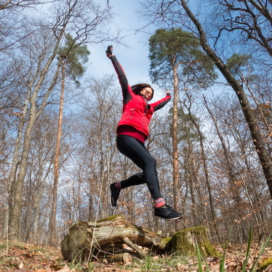 Woman jumping in the woods wearing outdoorsy clothing