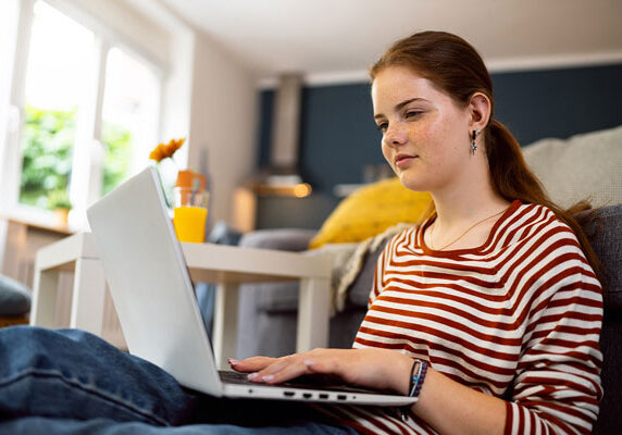 Teenage girl, using a laptop, while sitting on the floor in the living room