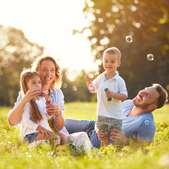 Family sitting together in a green field blowing bubbles and having fun.