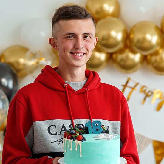 A teenage boy holding an 18th Birthday cake holding