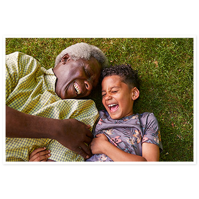 A grandfather and grandson laugh together, laying in the grass.