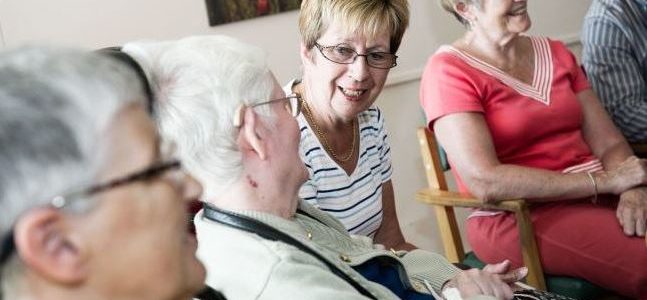 Elderly women sit in a row, chatting