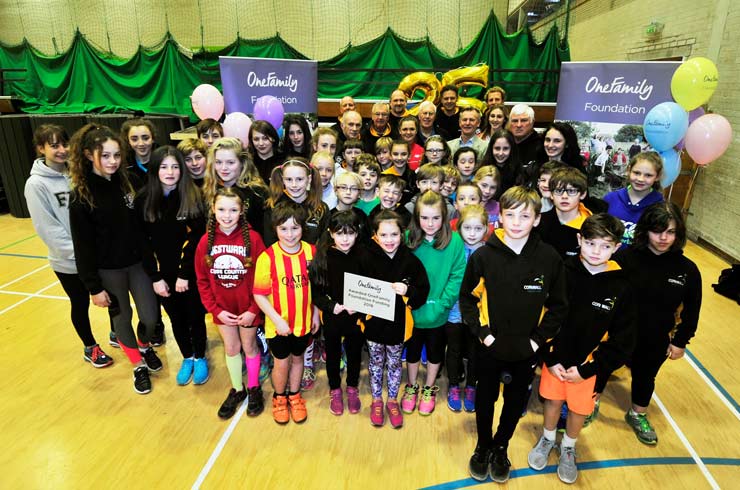 Cornwall Athletics Club stand in their gym with OneFamily Foundation banners in the background