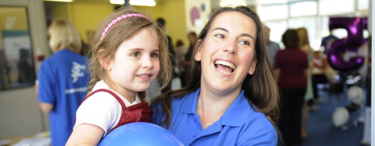 A smiling women carries a little girl