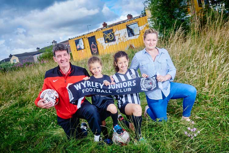 A man, a woman and two girls hold up a Wyrley Juniors Football Club scarf