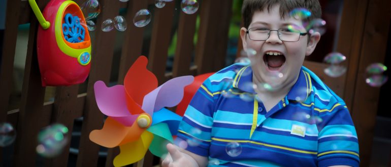 alistair-mclennan A boy in glasses laughs at bubbles floating in the air