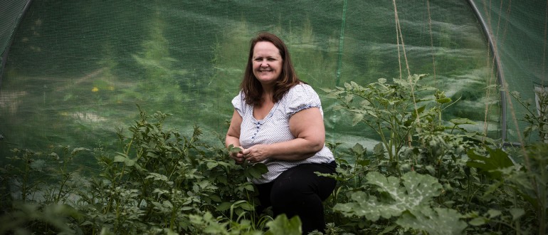 A lady crouches amongst her crop in a polytunnel.