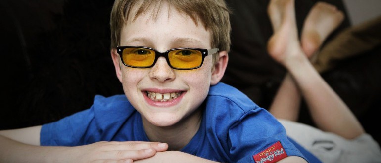 A little boy in glasses smiles to the camera.
