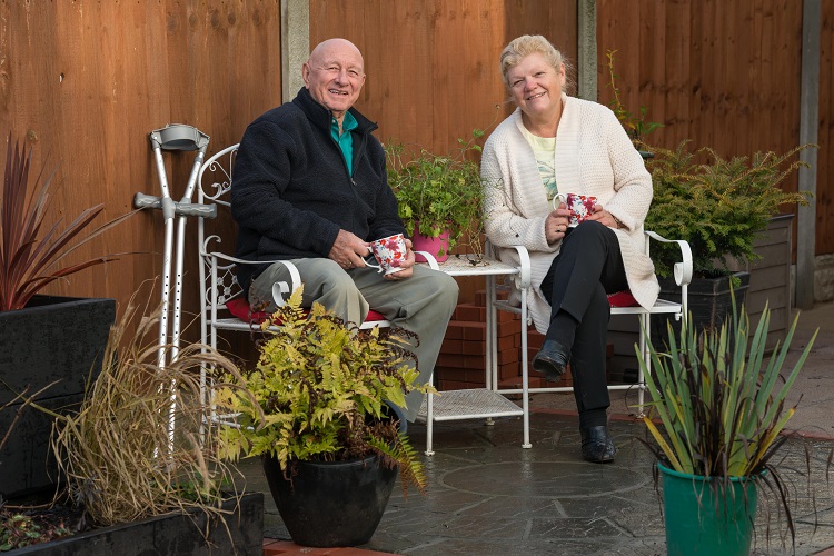 irene-and-frank An elderly man and woman sit on garden furniture, drinking tea.