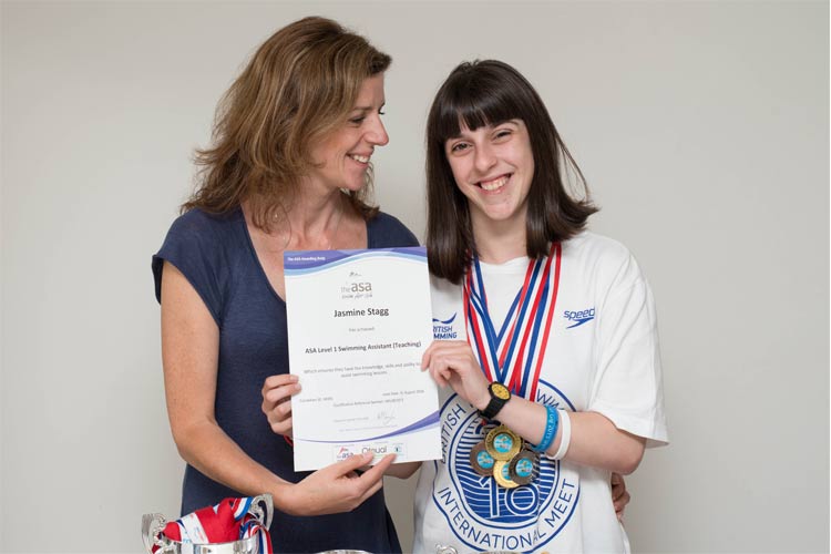 A women and a young girl stand holding a certificate. The girl wears several medals.