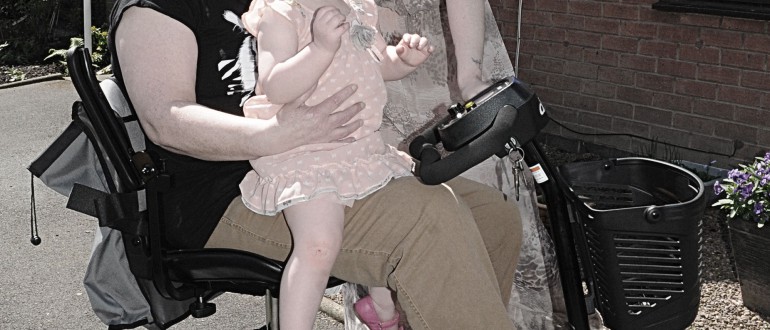 Close up of a little girl sitting on the lap of a person in a mobility scooter