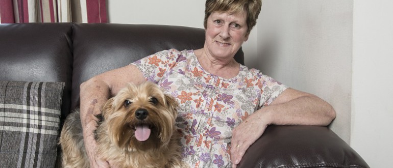 A lady sits on a sofa with a smiley dog.