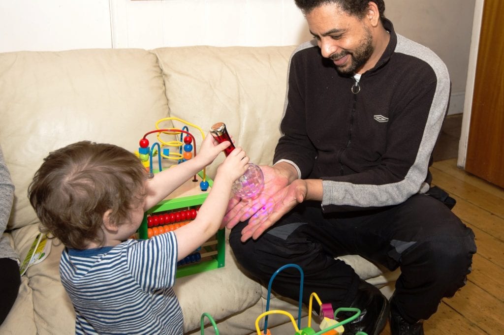 A man in a tracksuit plays with a little boy who is holding a light toy