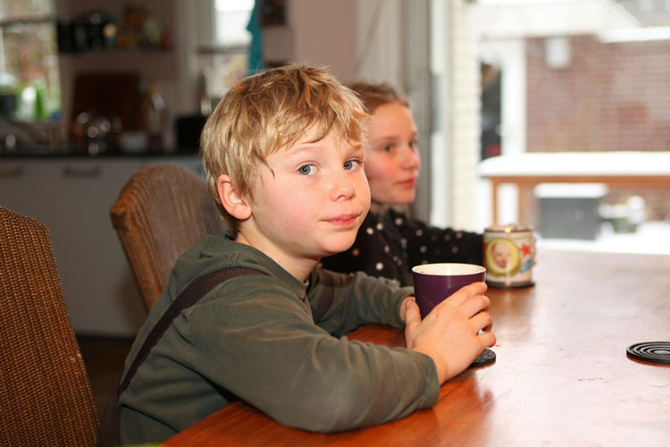 A little boy and little girl sit at a table holding mugs.