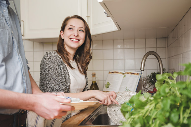 A pretty girl smiles at a man while doing the dishes.