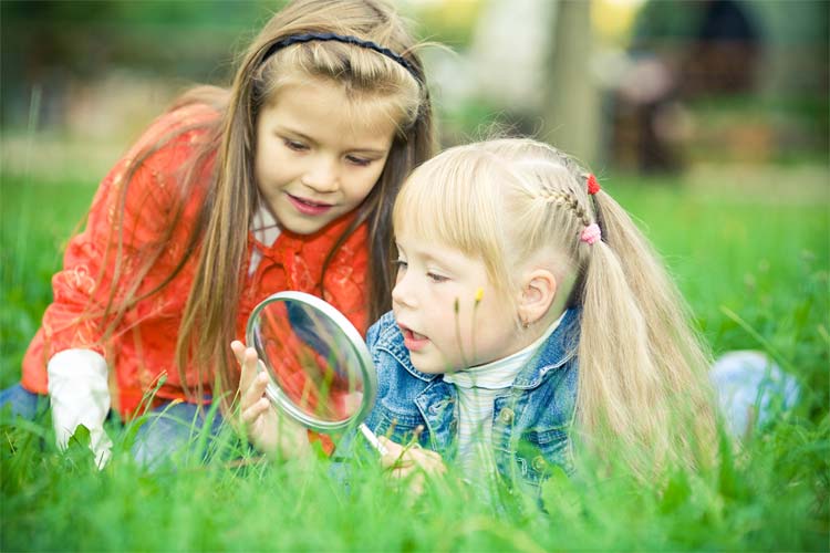 Two girls lie in the grass looking through a magnifying glass.