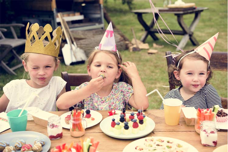 Children wearing party hats, with party food laid out on a table in front of them.