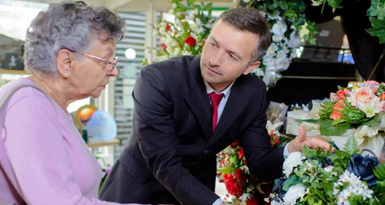A flower-seller shows a bouquet to an older woman.