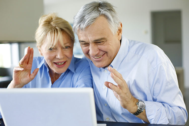 A grey-haired couple looking excitedly at their laptop screen.