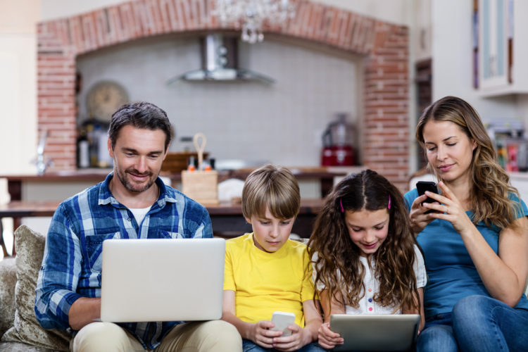 Four members of a family, all sitting on their laptops and mobile phones.