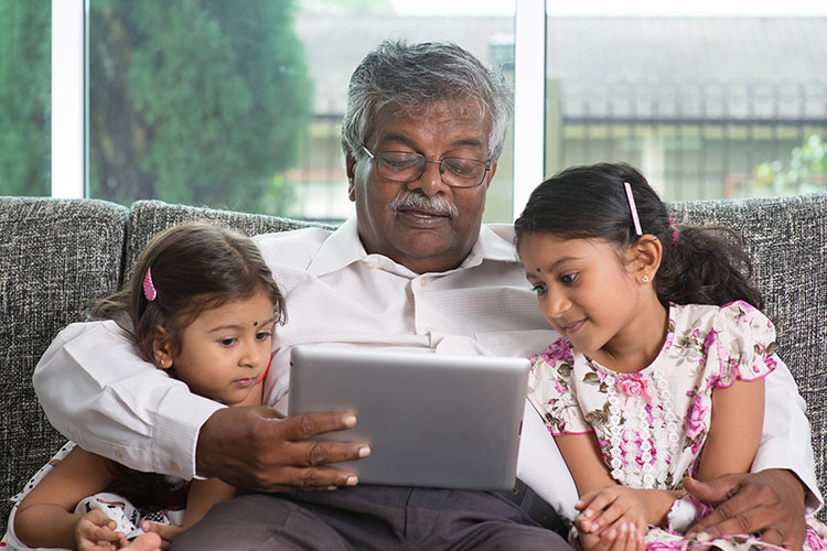 A man looking at his tablet computer with his granddaughters on either arm.