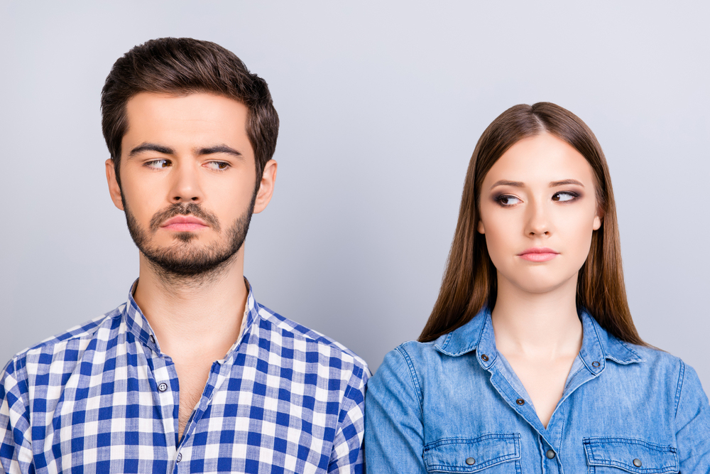 Young adult couple looking at each other suspiciously
