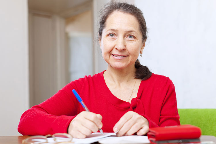 A lady in a red top writing in a notebook with a biro pen.