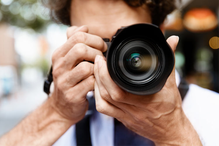 Close-up of a person with a camera, aiming directly at us.