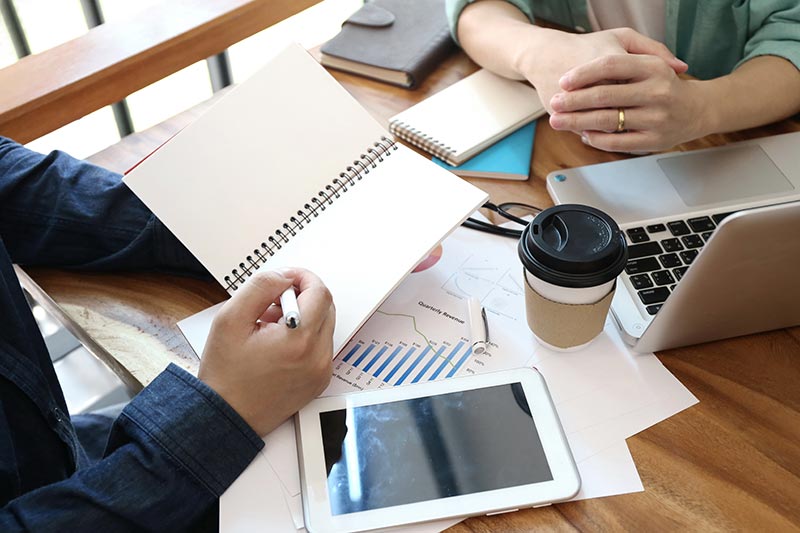 Two people looking at graphs and figures taking notes