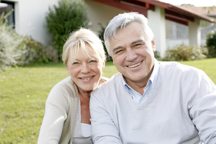 An older couple sitting in their garden, smiling.