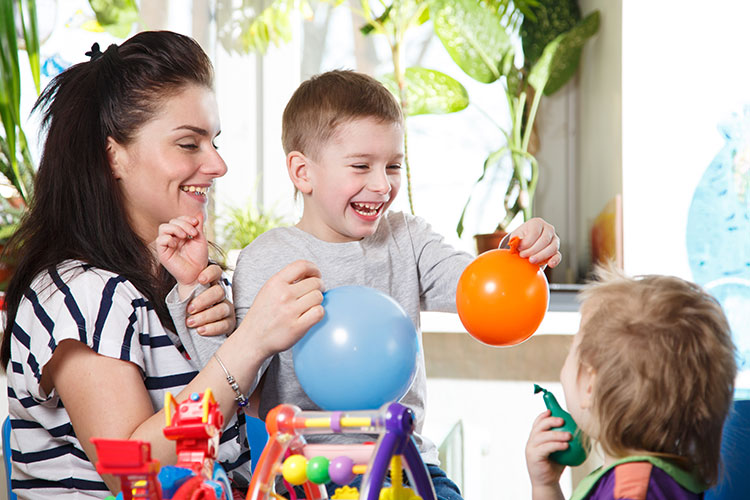 A woman and her son use balloons to entertain a toddler.