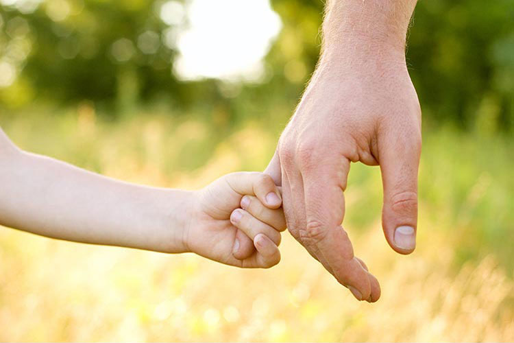 Close-up of a child's hand holding the pinky finger of an adult.