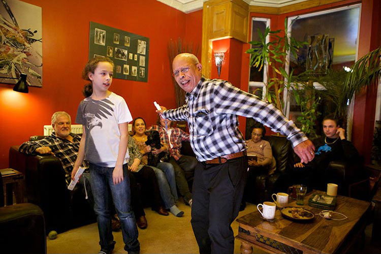 A man and his granddaughter playing on a Wii while the rest of the family look on.