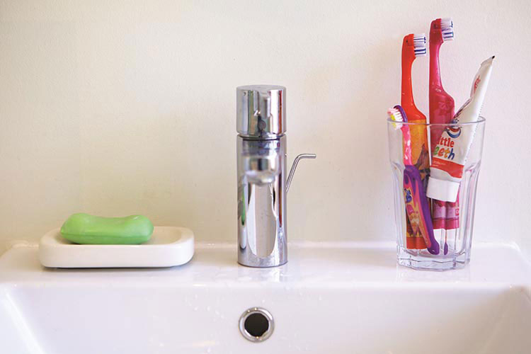 Close up of a bathroom tap, with a bar of soap on one side and a glass with toothbrushes and toothpaste on the other.