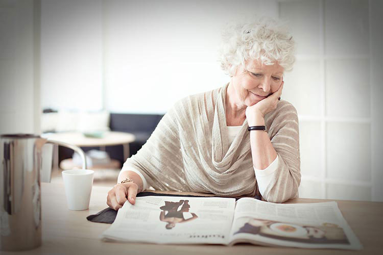 Older lady sitting at the dinner table, reading a newspaper.