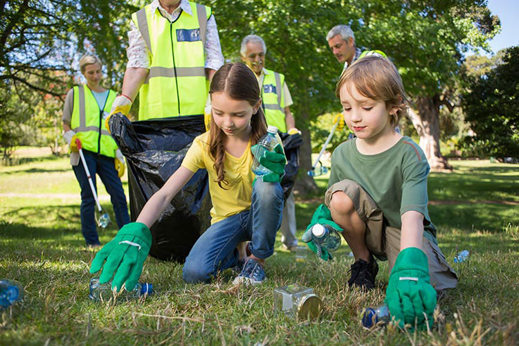 Two children wearing green gloves, picking up rubbish in a park.